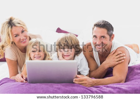 Smiling family using laptop on a bed