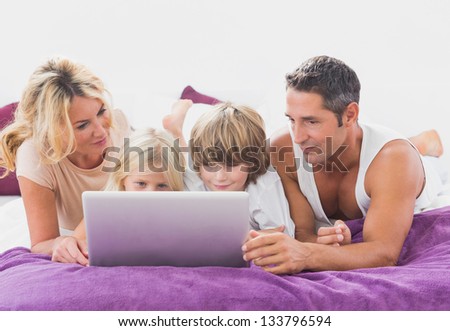Family using together a laptop on a bed