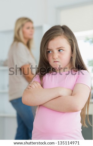 Little girl looking angry in the kitchen with mother in background