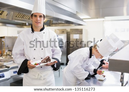 Chef\'s preparing deserts with one chef presenting his dish in the kitchen
