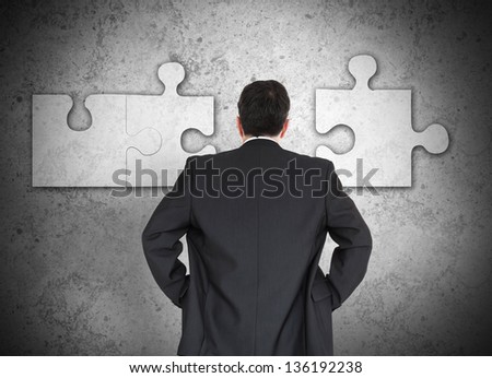Businessman figuring out missing piece of the puzzle on grey wall