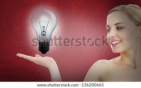 Smiling woman with light bulb inside her hand against digital circuit board