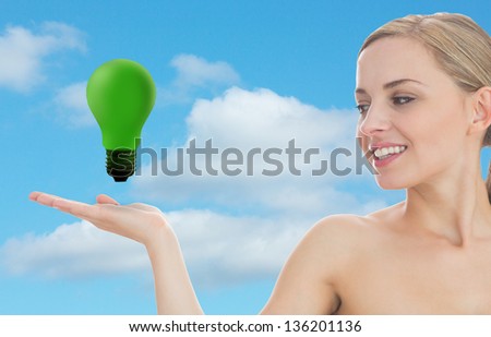 Smiling woman looking at green light bulb against sky background