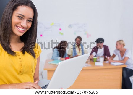 Happy woman using laptop with creative team working behind her in the office