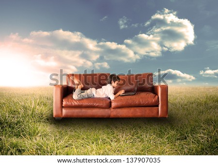 Child using laptop on couch in sunny field in the countryside
