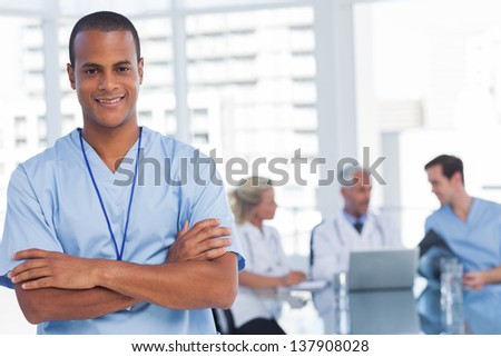 Smiling doctor with arms crossed standing in front of his team