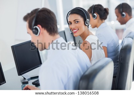Attractive call centre employee looking over shoulder while wearing a headset