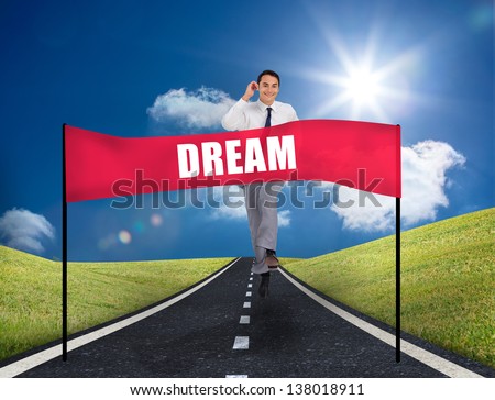Smiling young businessman running on a road with a banner with dream written on it
