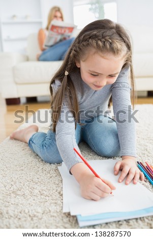 Little girl drawing on paper sitting on floor with mother reading newspaper on the couch