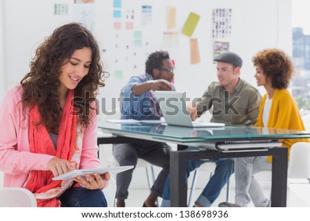 Smiling designer using digital tablet with team at work behind her
