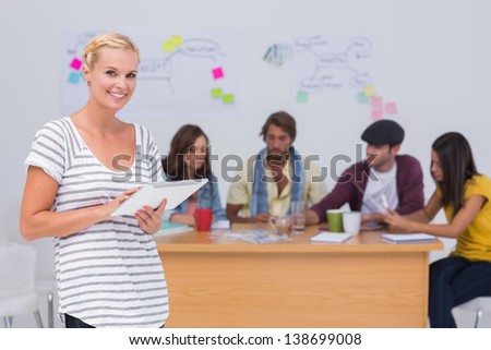 Happy editor using tablet pc as team works behind her at desk in the office