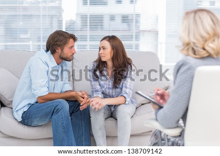 Couple looking to each other during therapy session while therapist watches