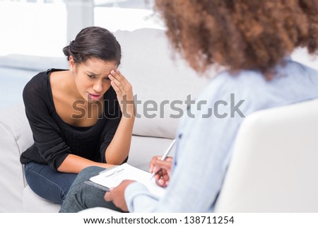 Woman crying on sofa during therapy session while therapist is taking notes Woman crying on sofa during therapy session while therapist is taking notes
