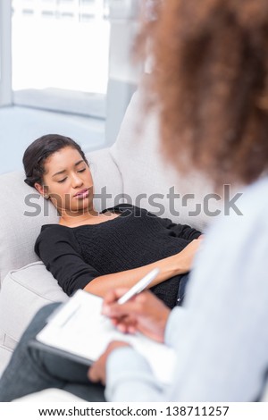 Woman lying on sofa during therapy session with therapist taking notes