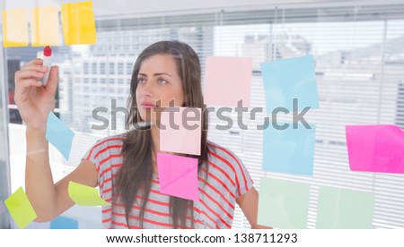 Young woman writing on sticky note in creative office