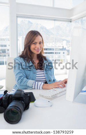 Cheerful photo editor working on computer at her desk with camera and graphics tablet