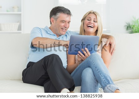 Husband and wife laughing at tablet pc on the sofa