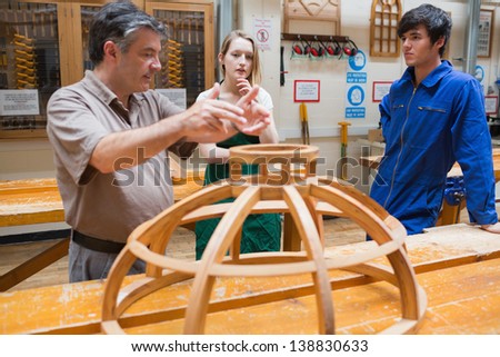 Teacher explaining a structure to two students while standing in a woodwork class