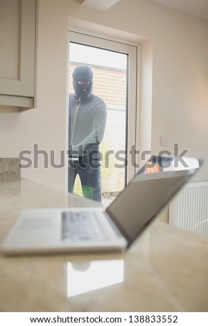 Burglar looking at laptop through the window of kitchen