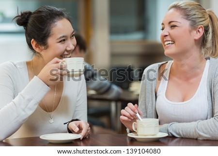 Two students having fun while sitting in college coffee shop and drinking coffee