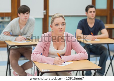 Three students sitting at desks in a classroom listening and about to take notes