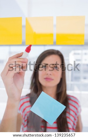 Young woman writing on sticky note in bright creative office