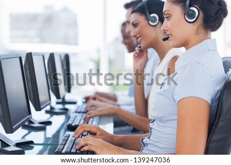 Call centre workers sitting in line while helping people on computers