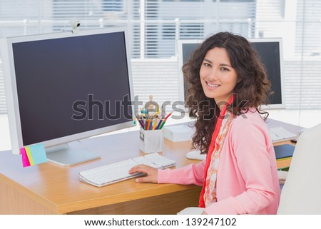 Woman working in a creative office and smiling at camera at her desk with computer