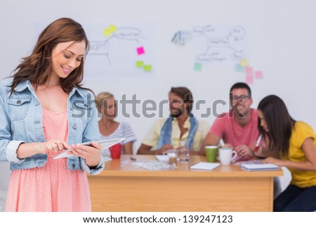 Smiling oman using tablet with creative team working behind her in the offices
