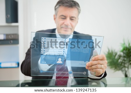 Businessman using futuristic touchscreen to view social network profile in his office