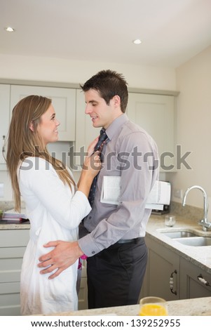 Woman fixing tie of husband before work in kitchen