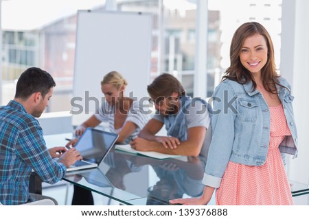 Team having meeting with one woman standing and smiling at camera in bright office