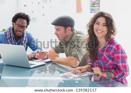 Creative team working together with one smiling at camera at desk in office