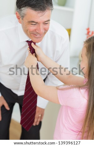 Father leaning down to let daughter fix his tie at home before work