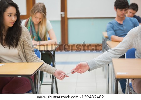 Two students sitting at a table in a classroom cheating while doing a test and