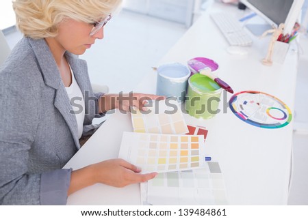 Serious interior designer looking at colour charts with paint pots and colour wheel on her desk