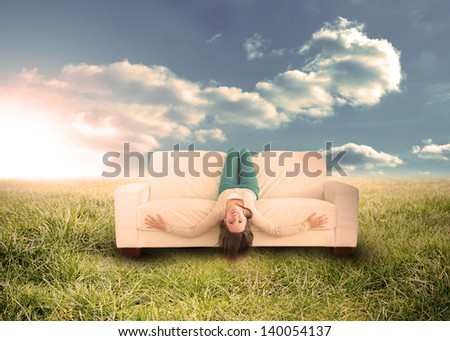 Silly woman sitting upside down on couch in sunny field in countryside