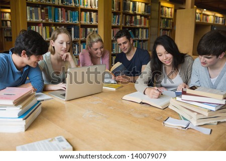 Students Sitting At A Table In A Library While Learning And Working On A Laptop