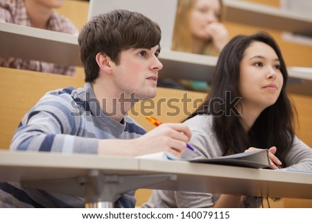 Students sitting in a lecture hall while studying and listening to the teacher