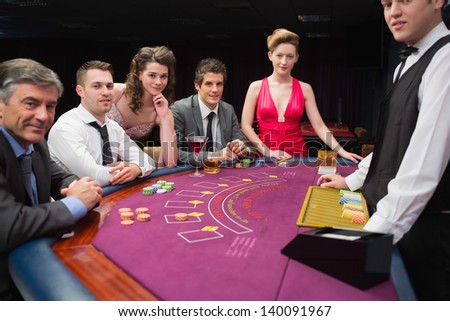People are sitting at the blackjack  table smiling at the casino