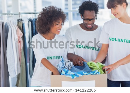 Cheerful volunteers taking out clothes from a donation box in their office