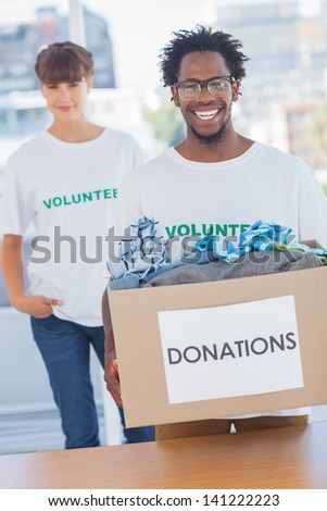 Handsome man holding donation box full of clothes next to a colleague