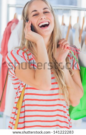 Blonde woman laughing in a clothing store while she is on the phone