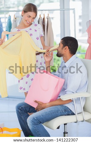 Woman showing clothes to her boyfriend who is sitting in a boutique