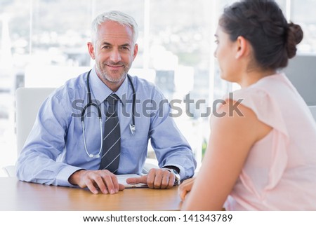 Attractive doctor sitting in front of patient in the office at desk