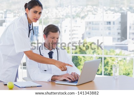 Doctor pointing at the laptop of a colleague in his office