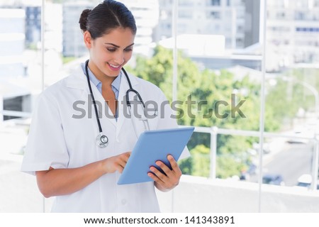 Smiling young doctor using tablet pc by windows