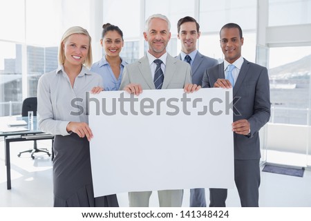 Business team holding large blank poster and smiling at camera