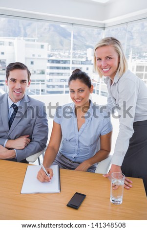 Business people at desk with notepad smiling at camera in the office
