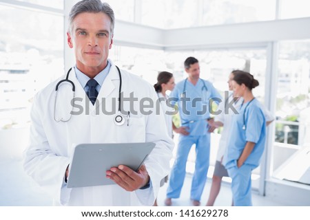 Serious doctor holding clipboard in front of his medical team